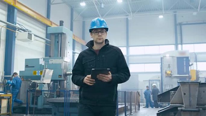 戴着安全帽的工厂工人正在走路和使用平板电脑。