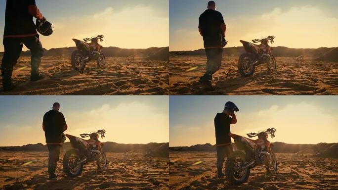 低角度拍摄的专业摩托车越野车司机戴上他的头盔和准备骑他的FMX土地车在采石场沙地。