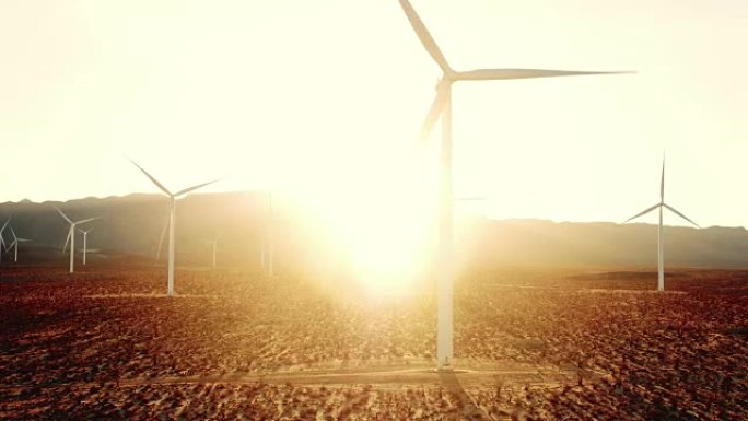 日落时带有透镜耀斑的沙漠中孤立的风车涡轮机的鸟瞰图