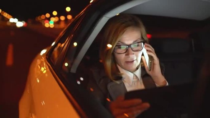 女商人在豪华轿车后座上使用数字平板电脑时在电话上聊天