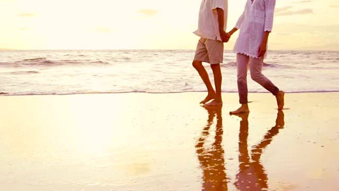 年长的夫妇握着手，在日落时沿着海滩走，弄湿了脚。