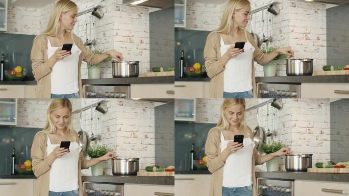 愉快的女人站在厨房前，用智能手机。她在锅里搅拌一些东西。