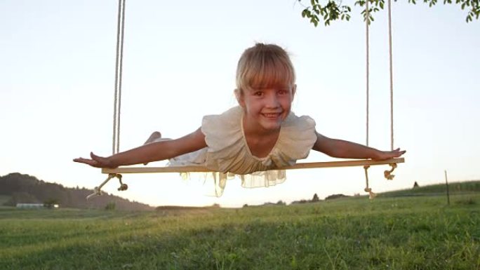 慢动作肖像: 快乐微笑的小女孩假装自己在秋千上飞翔