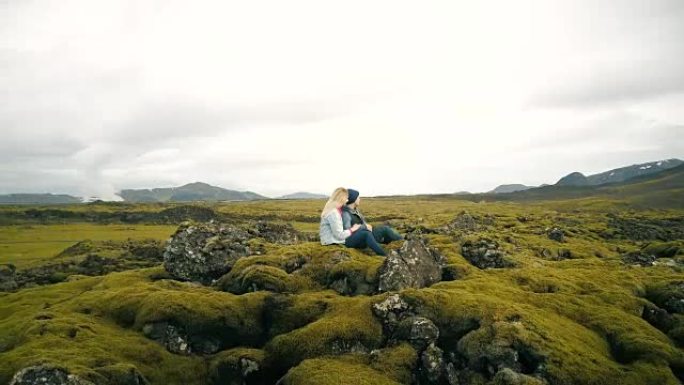年轻美丽的夫妇坐在冰岛享受熔岩场景观的鸟瞰图。直升机飞来飞去