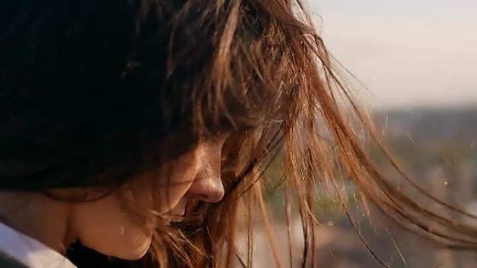 风吹起长长的黑发。女孩低着头站在屋顶上。特写。慢动作