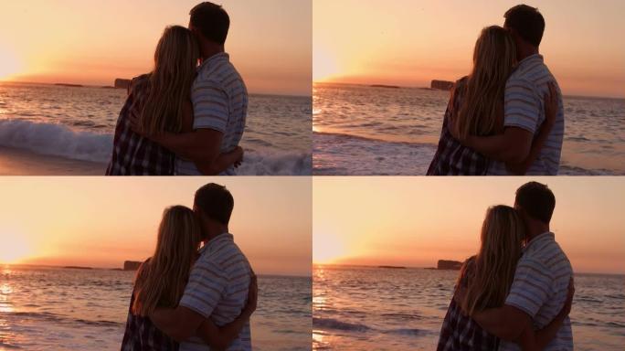 可爱的情侣在海滩上日落时拥抱