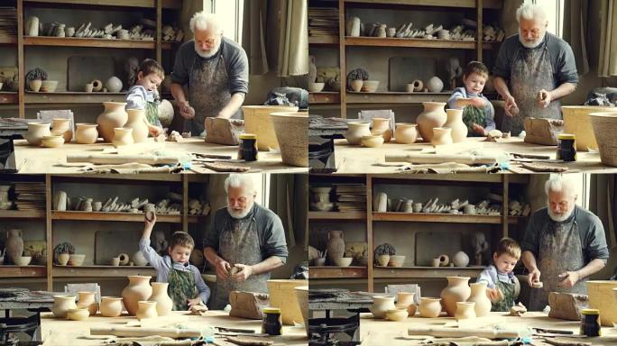 开朗的小男孩在波特的工作室里帮助他的祖父时，正在将黏土扔在工作台上。快乐的童年、家庭传统和爱好概念。