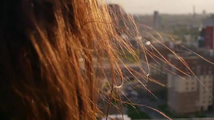 后视图。特写风吹起长长的黑发美丽的年轻女性。日落时站在屋顶上的女孩。慢mo