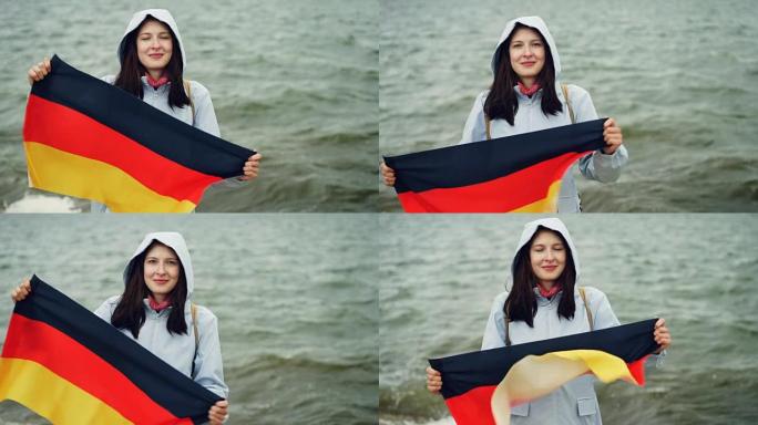 慢动作肖像美丽的德国妇女骄傲的公民举着德国的官方旗帜，并移动它站在河岸上与幸福的微笑。
