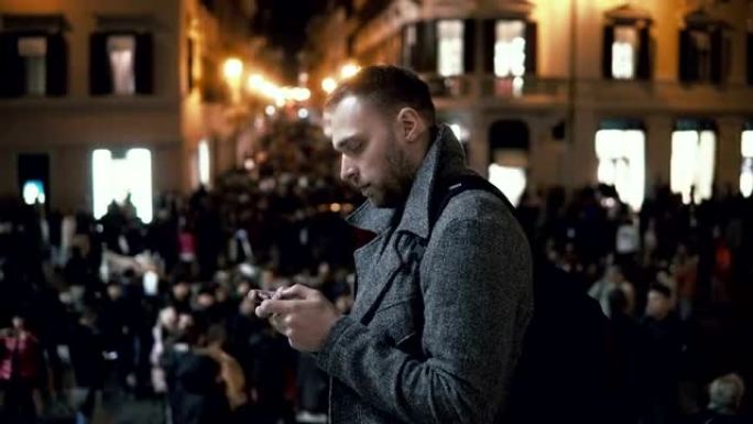 晚上在市中心的年轻人。男性使用智能手机站在市中心的广场上