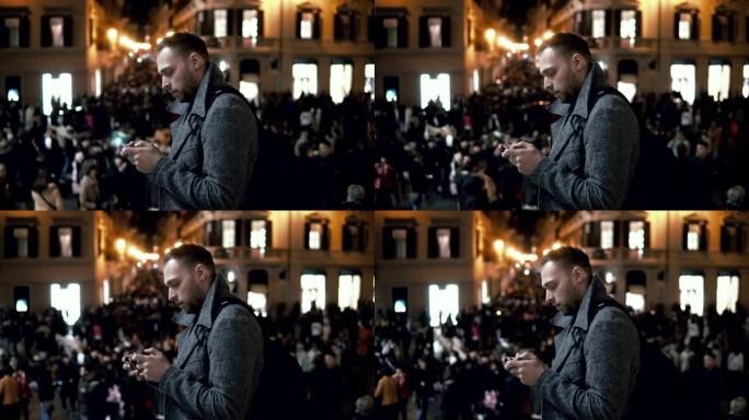 晚上在市中心的年轻人。男性使用智能手机站在市中心的广场上