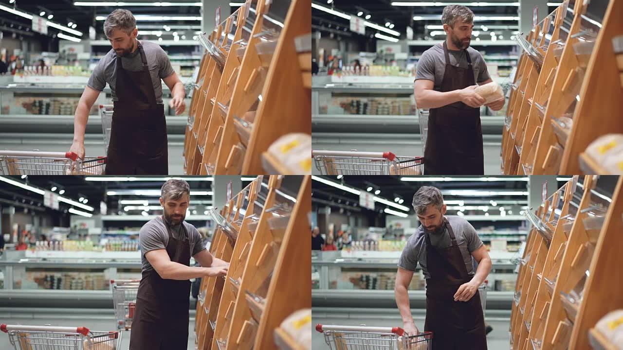 大型超市的男性员工正在从购物车中取出新鲜面包，并将其放在面包店部门的货架上。卖食物和人的概念。