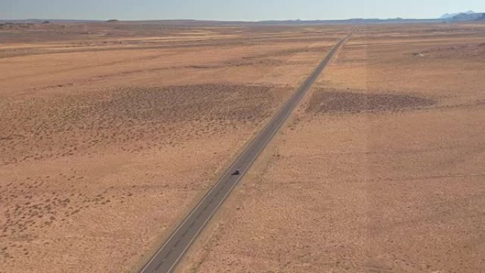 空中: 黑色汽车在空旷的道路上行驶，穿越无尽的沙漠山谷