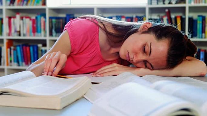 疲倦的女学生在做作业时睡在图书馆
