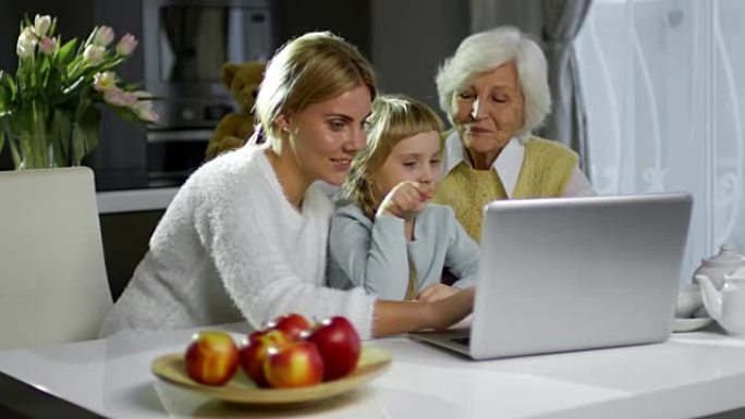 欢乐的妈妈，奶奶和小女孩在家里使用笔记本电脑