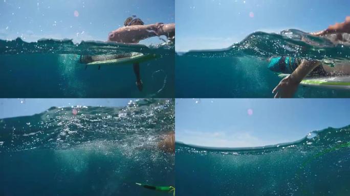 水下慢动作: 微笑的冲浪者在广阔的蓝色海洋中划桨
