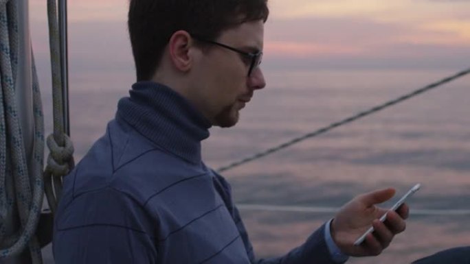 日落时，一名男子正在海里的帆船上寻找和使用电话。