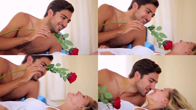 男人在床上用玫瑰挠他的金发女友