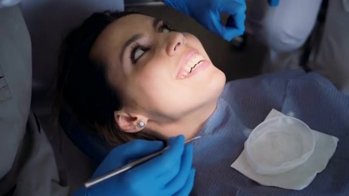 去看牙医的年轻女子的肖像。女性坐在牙科椅上聊天。女孩用舌头碰牙齿