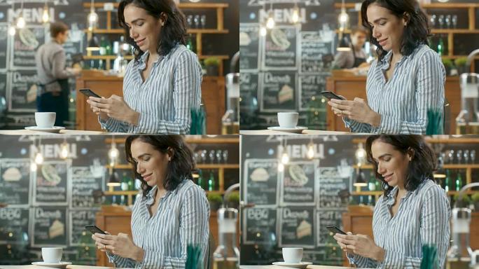 美丽的女人坐在咖啡馆里使用智能手机。她在给朋友或爱人发消息时微笑。放在她的桌上杯子里。在后台忙碌的时