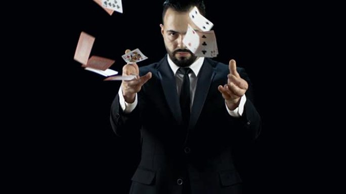 穿着深色西装的专业年轻魔术师以慢动作向空中投掷两束纸牌。背景是黑色的。