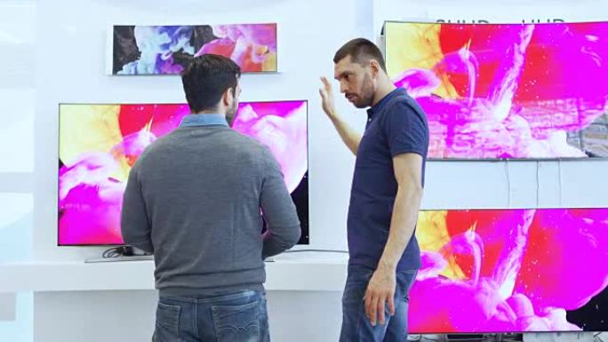 在电子商店中，专业顾问向年轻人展示了最新的4K UHD电视，他们讨论了规格以及哪种型号最适合年轻人的