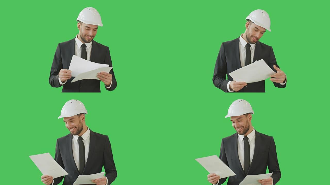 一个成功的商人戴着安全帽，愉快地浏览图表的中景。在绿屏背景上拍摄。