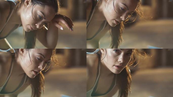 一个美丽的运动女人的特写镜头用手擦拭额头上的汗水，看着相机。经过密集的交叉健身运动，她很累。