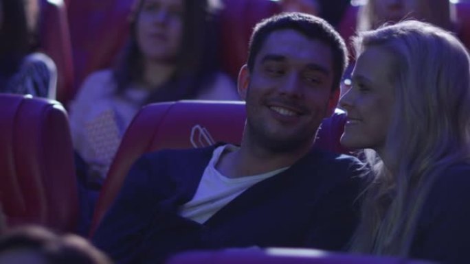 年轻的浪漫情侣在电影院看电影放映时亲热接吻。