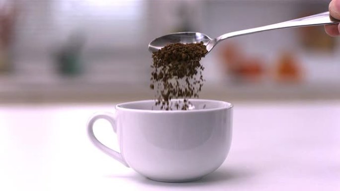 将速溶咖啡从茶匙倒入白色杯子中