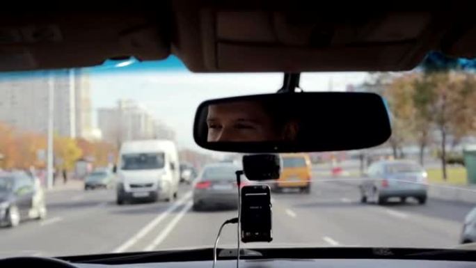 在城市繁忙的道路上开车时，微笑着的人在镜子里。英俊的男人的脸。开车旅行