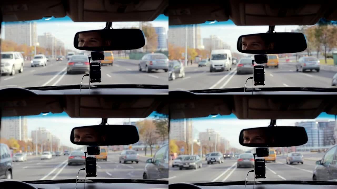 在城市繁忙的道路上开车时，微笑着的人在镜子里。英俊的男人的脸。开车旅行