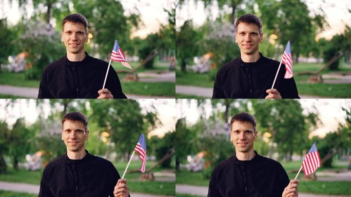 穿着便服的迷人男人的慢动作肖像挥舞着美国国旗，微笑着看着相机。快乐的人，骄傲的公民，国家和自然的概念