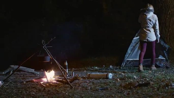女孩从燃烧的篝火中站起来，晚上去帐篷。