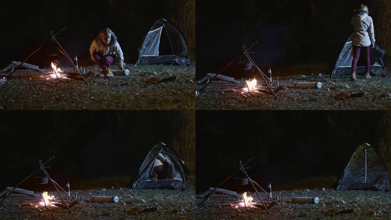 女孩从燃烧的篝火中站起来，晚上去帐篷。