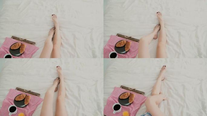 女人脚的特写镜头。年轻女孩躺在床上，在客厅吃早餐