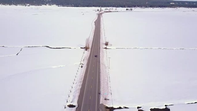 空中4K: 一辆汽车在高速公路上行驶，穿过积雪覆盖的田野