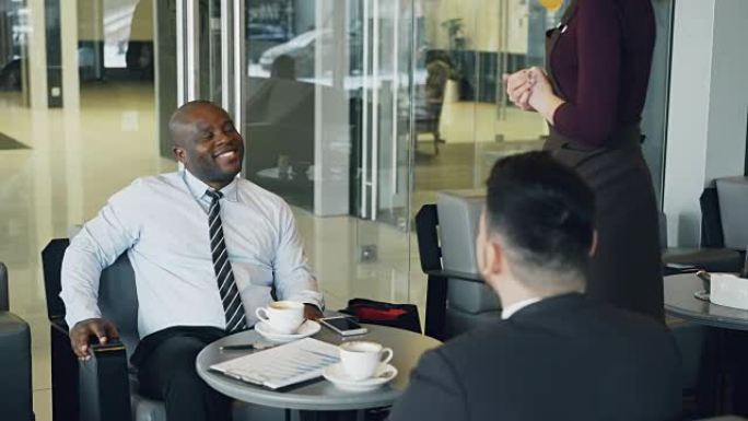 穿着正装的成功的非洲裔美国商人微笑着，与他在咖啡馆的高加索同事讨论财务报告。年轻的女服务员带来咖啡杯