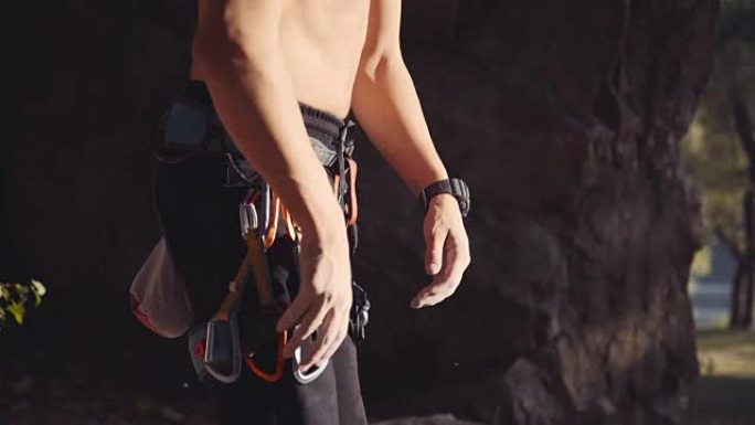 赤裸上身的攀岩者拿着钩环，双手沾满粉笔