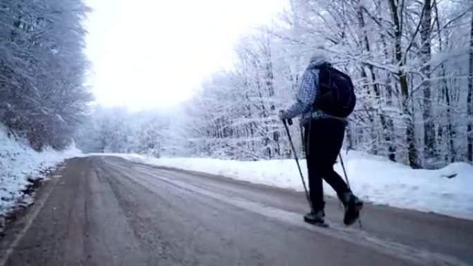 女徒步旅行者走在白雪皑皑的森林边的一条路上