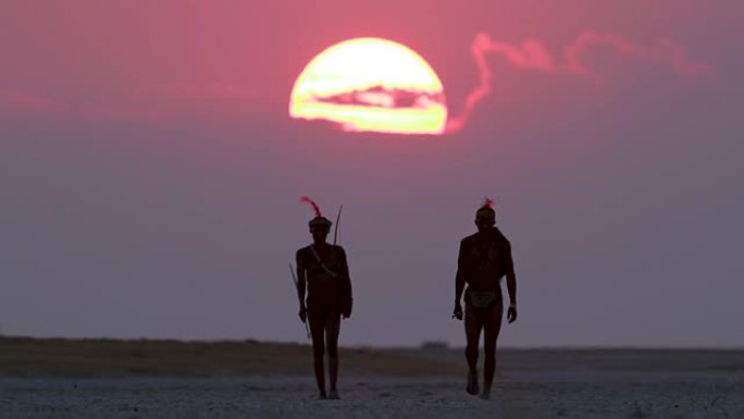 博茨瓦纳，两名圣布须曼人正穿过Makgadikgadi pan，身后是夕阳西下的红色天空