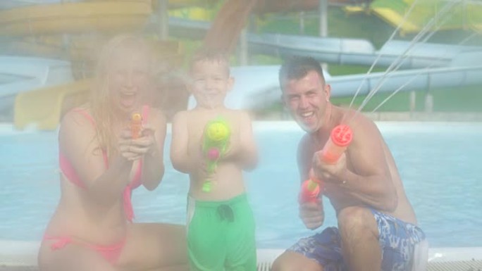 慢动作: 微笑的年轻家庭进行一场有趣的水上战斗，快乐的母亲，父亲和儿子用水枪射击并将水直接喷入相机