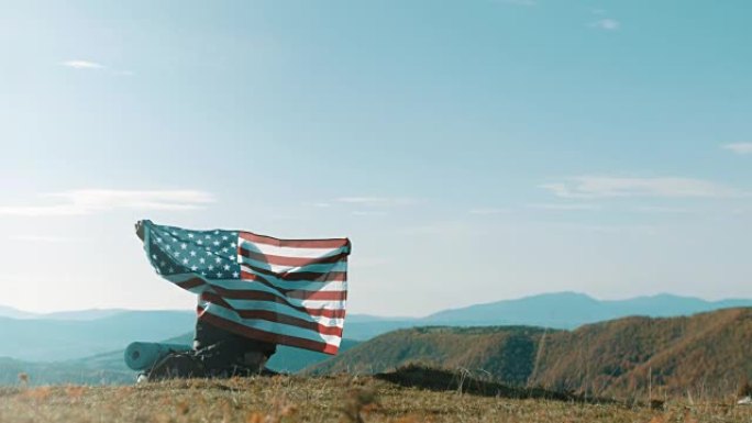 男子坐在山顶上，举着美国国旗