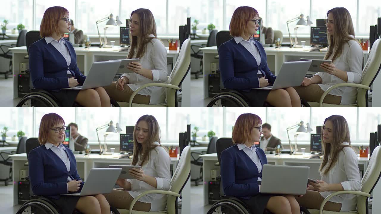 使用平板电脑并与残疾女同事交谈的年轻女子