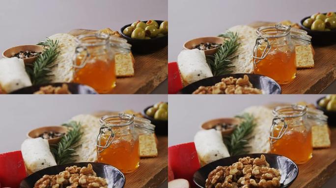 一碗绿橄榄，面包，果酱，迷迭香药草，奶酪和核桃放在木板上