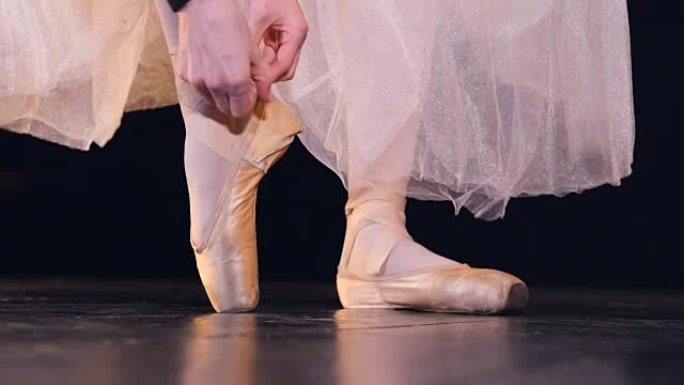 女性的手在芭蕾舞鞋上系上两条丝带。