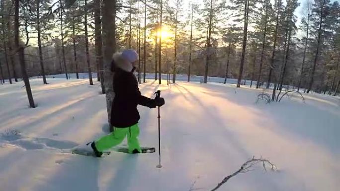 特写镜头年轻女子雪鞋在金色冬季日出时穿过雪景