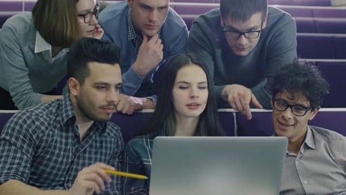 一群男女学生坐在大学教室里，看着一台笔记本电脑。