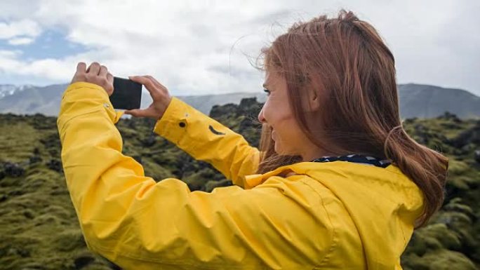 穿着黄色雨衣的游客在火山景观上拍摄苔藓覆盖
