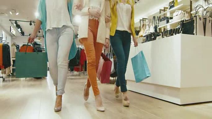 低矮的女性双腿穿过百货商店，穿着彩色衣服带着购物袋走向相机。